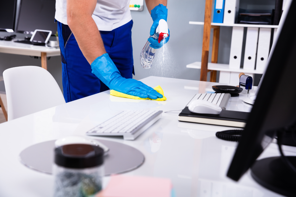 Erfahrene Reinigungskraft reinigt die Oberfläche eine Schreibtisches in einem Büro